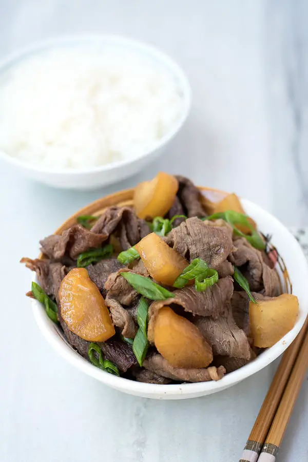 Bowl of beef with daikon radish topped with sliced green onion, with a bowl of rice. 
