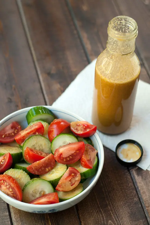 A bottle of homemade sesame dressing next to a bowl of cucumbers and tomatoes. Sesame Dressing