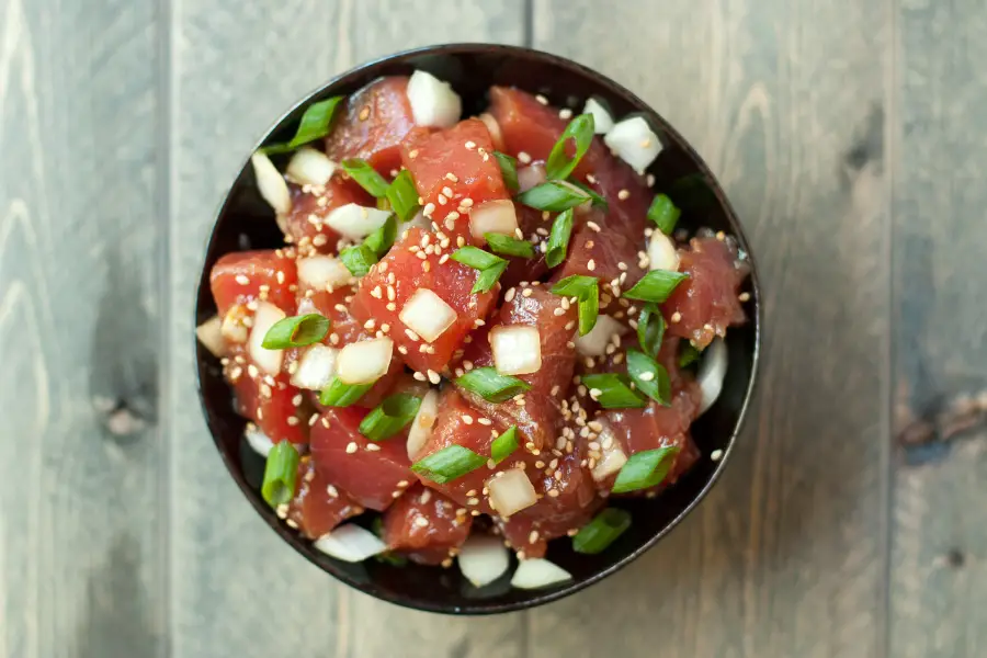 Top view of a bowl of ahi poke, garnished with sliced green onions and toasted sesame seeds. 