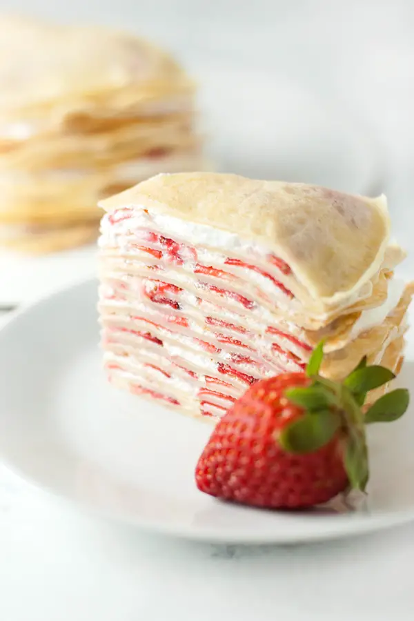 Slice of strawberry crepe cake, with a strawberry in the foreground.