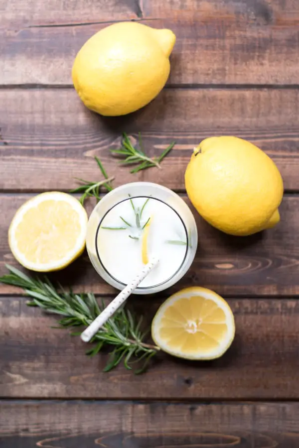 Top view of a glass of rosemary lemon cream soda with lemons and sprigs of fresh rosemary. 