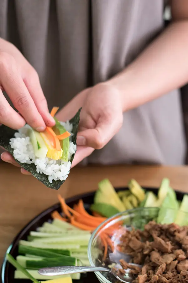 Rolling a sushi hand roll with avocado, carrots, egg, and cucumber.