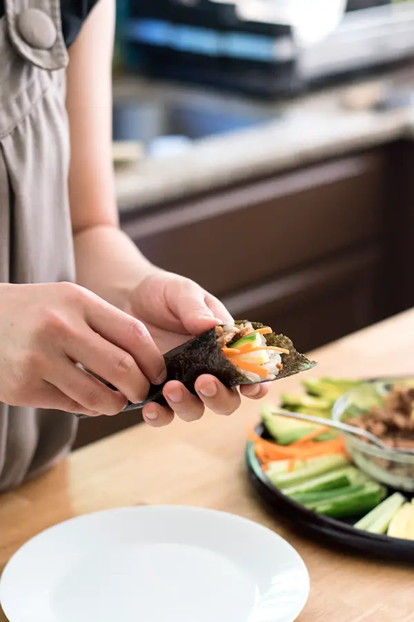 Finished rolling a sushi hand roll filled with tuna, carrots, and cucumber. 