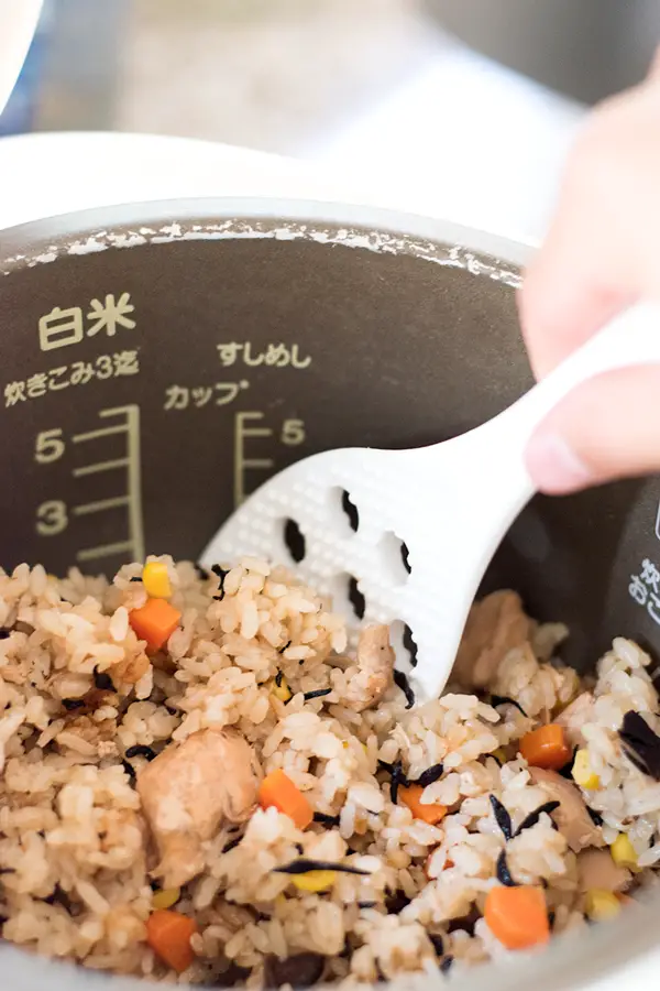 Tuna takikomi rice in rice cooker bowl, being scooped with rice paddle. 