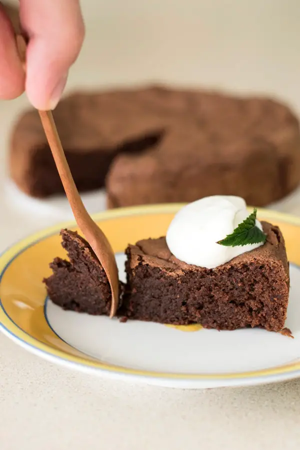 Taking a bite from a French chocolate cake topped with dollop of cream using wooden fork.