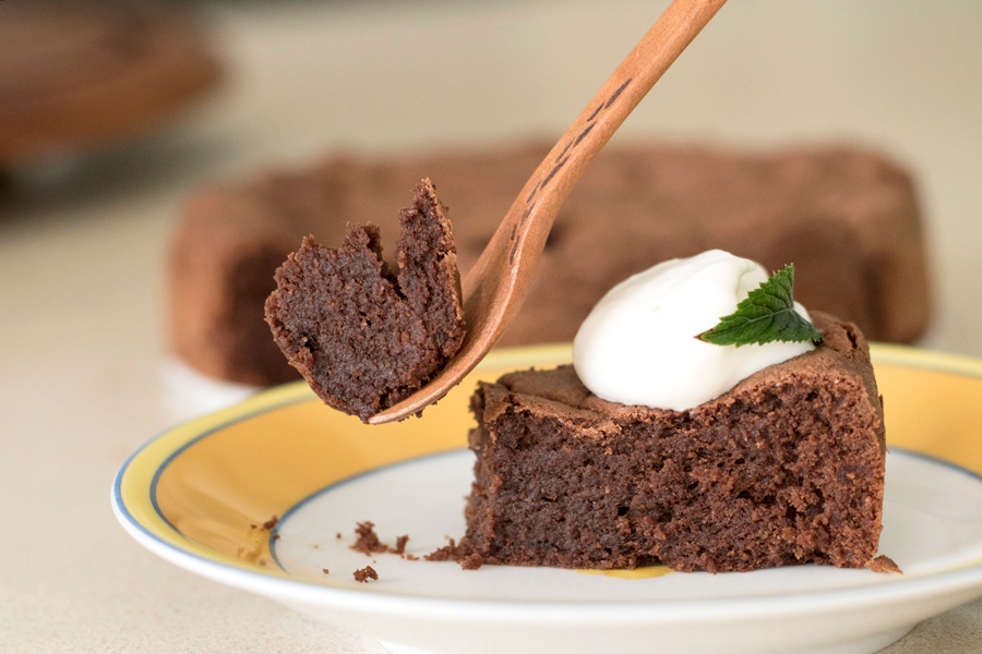 Fork lifting up a piece of gateau topped with dollop of whipped cream and mint leaf. 