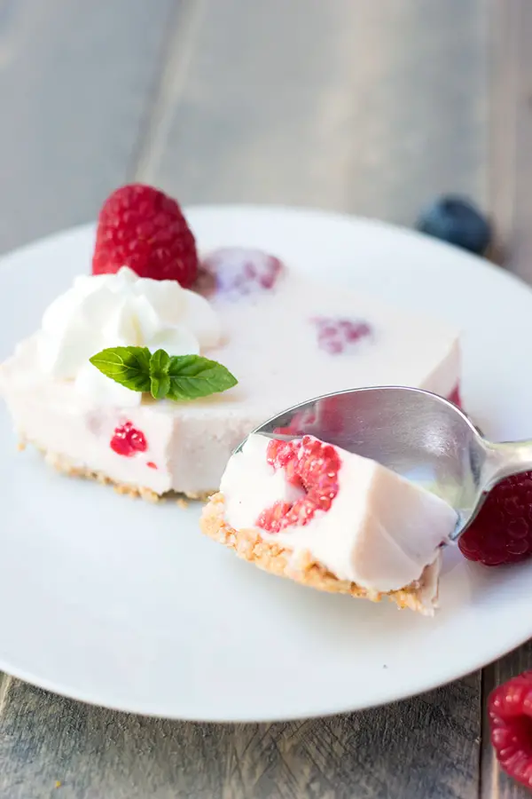 Taking a bite from a raspberry no bake cheesecake bar topped with whipped cream and mint garnish.