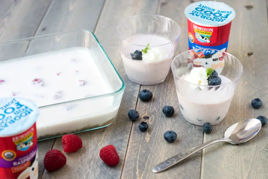 Unsliced raspberry no bake yogurt cheesecake with two blueberry no bake yogurt cheesecake cups.