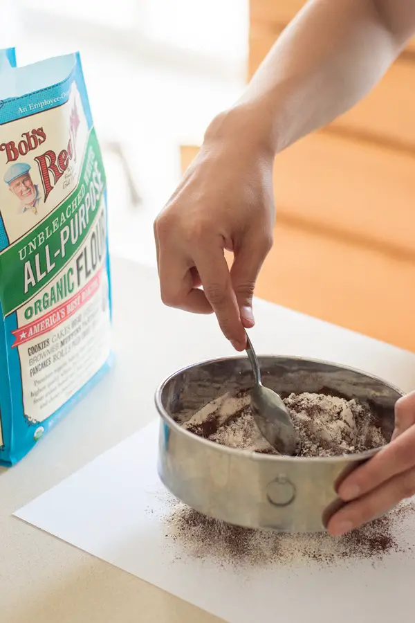 Sifting Bob's Red Mill all purpose flour with cocoa powder onto a piece of paper.