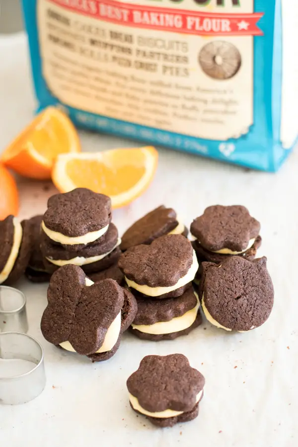 Chocolate orange sandwich cookies stacked up with orange slices and Bob's Red Mill flour in background