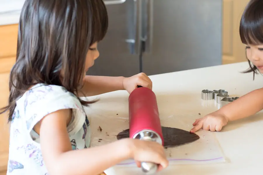 Kids rolling out chocolate sandwich cookie dough inside a gallon Ziploc bag.