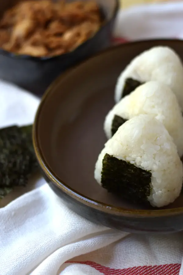 3 Tuna mayo onigiri lined up with a bowl of tuna in the background.