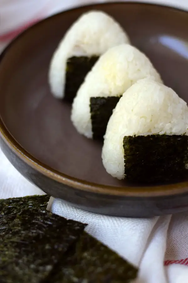 3 tuna mayo onigiri lined up with some seaweed on the side.