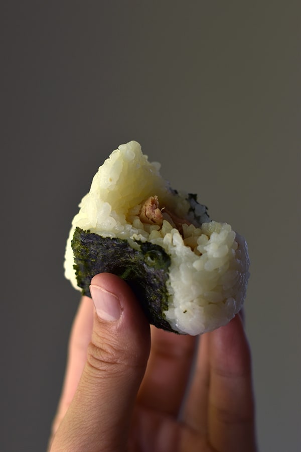 Hand holding a tuna mayo onigiri with a bite taken out of it. 