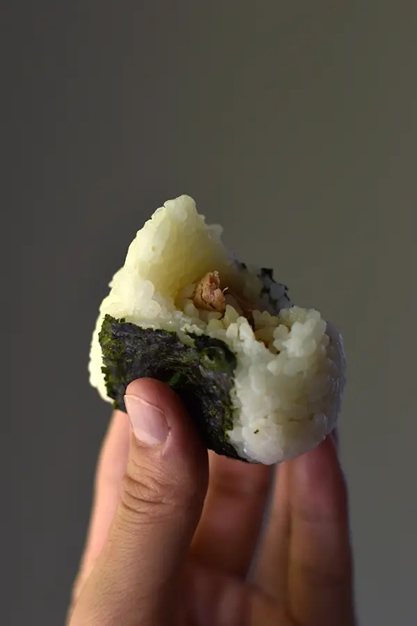 Hand holding a tuna mayo onigiri with a bite taken out of it.