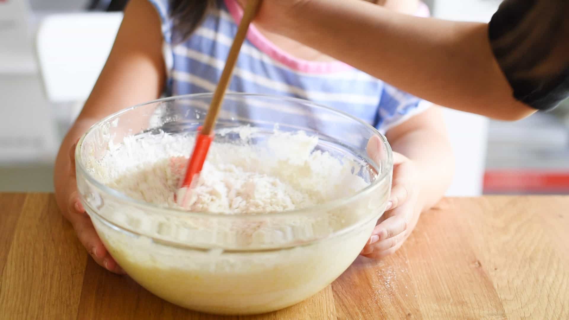 Holding mixing bowl and stirring in flour with a rubber spatula