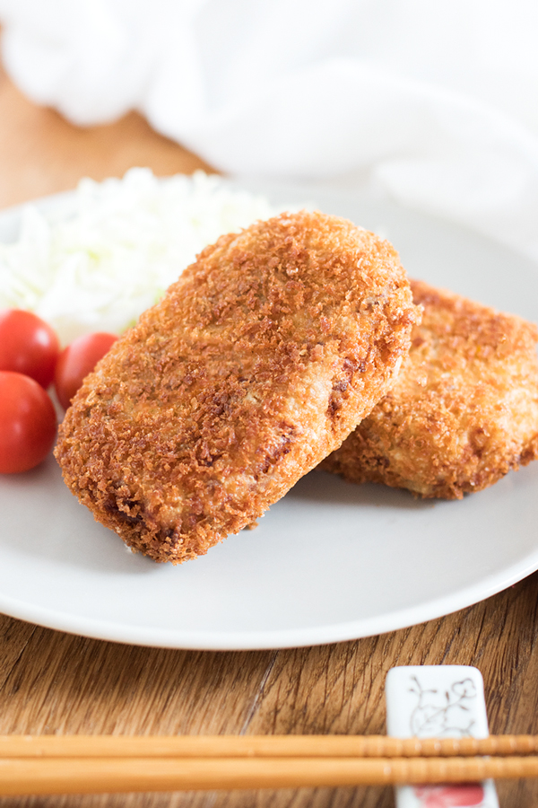 Korokke is the Japanese take on the French croquette, and is a very popular dish in Japan. Patties of mashed potato and ground beef are coated in panko and deep fried. Served with a delicious sauce, this comfort food cannot be beat! Potato croquette, Japanese Korokke on a dish with cherry tomatoes and shredded cabbage.