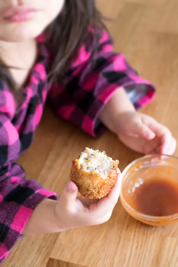 Little girl holding a round korokke dipped in sauce. 